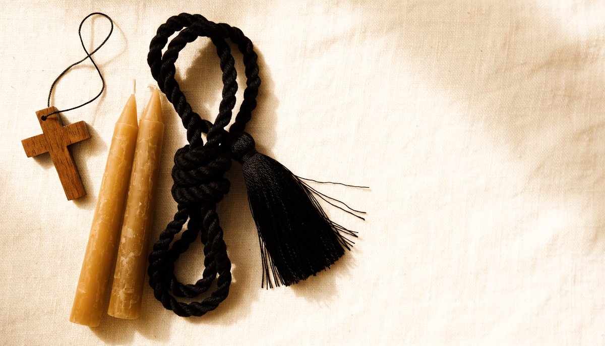 Prayer rope, wooden cross and beeswax candles on cream linen