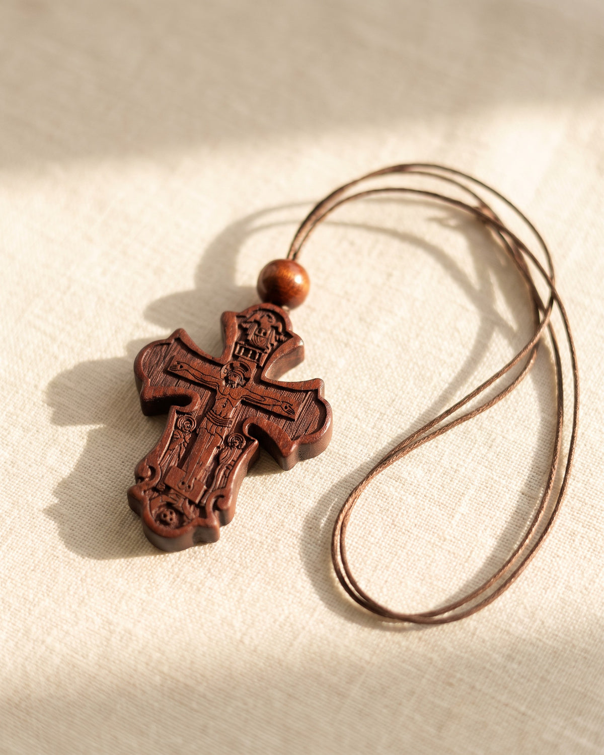 The carved cross pendant resting on cream linen